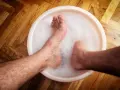 A person's feet soaking in a bubbly foot bath on a wooden floor.