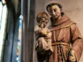 A statue shows what friars wear: brown robes, a cord belt, and a rosary. A child with a halo holds fruit.
