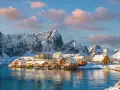 Snow-covered mountains frame a picturesque village with orange and white houses on stilts over the water, a scene from one of Europe's best winter destinations.
