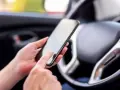 Ręce trzymają smartfon w samochodzie, obok kierownicy. Może to być pomocne, by dowiedzieć się, co to aux i jak podłączyć muzykę.