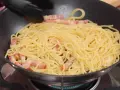 Espaguetis con trozos de panceta en una sartén, preparándose para unos deliciosos tallarines a la carbonara.