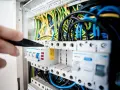 Ręka majstruje przy bezpiecznikach w rozdzielnicy, pokazując różne rodzaje instalacji elektrycznych.