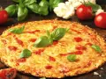 Pyszna pizza z kalafiora, z ciągnącym się serem i świeżą bazylią, otoczona pomidorami i różyczkami kalafiora.