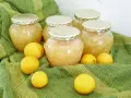 Plusieurs bocaux de confiture de citron maison, entourés de citrons frais, sur un tissu vert rayé.