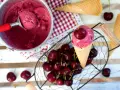 Ein Eisbecher mit Kirscheis, eine Kugel in einer Waffel, frische Kirschen und leere Waffeln.