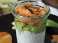 Leckerer Lachs Avocado Vorspeise im Glas, geschichtet mit cremiger Sauce und garniert mit Dill. Dazu geröstete Brotscheiben.