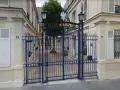 Brama do Ecole de Paris, ozdobiona złotymi detalami, prowadzi na dziedziniec z drzewem i ławką.