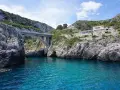 Ponte moderno su un mare cristallino, incastonato tra scogliere rocciose. Un luogo magico dove si incontrano i due mari in Puglia, con un ristorante panoramico sulla collina.