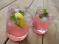 Två glas med rosa rabarberdrink, is, citron och mynta på träbord.