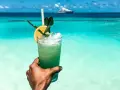 Orzeźwiający drink na plaży z widokiem na turkusowe morze i luksusowy jacht. Idealny moment relaksu.