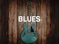 Eine teal-farbene E-Gitarre mit dem Wort "BLUES" darüber, auf rustikalem Holz Hintergrund.