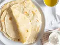 Piatto di piadine senza strutto, morbide e dorate, pronte per essere farcite. Accanto, una ciotolina d'olio e una di farina.