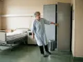 Ältere Frau im Krankenhaushemd, die sich an einer Tür festhält. Sie hatte einen Arbeitsunfall, ging aber nicht zum Arzt.