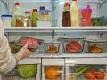 Mano colocando carne picada envasada en un refrigerador lleno de alimentos.