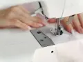 Dłonie szyjące podszewkę w nogawkach spodni na maszynie.