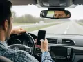 Mann am Steuer während der Probezeit, der auf sein Handy schaut. Eine gefährliche Ablenkung, die vermieden werden sollte.