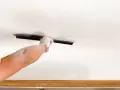 A dusty hand uses a trowel to texture a ceiling, demonstrating how to texture a ceiling for a fresh look.