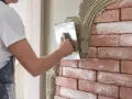 Un ouvrier applique de l'enduit sur une brique avec une truelle, créant une texture rustique.