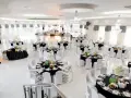 Elegancka sala weselna z czarnymi obrusami i białymi pokrowcami na krzesła. Stoły zastawione, gotowe na przyjęcie gości. Zastanawiasz się, ile za talerzyk na weselu?