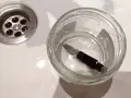 Pluma estilográfica sumergida en un frasco de vidrio con agua, junto a un desagüe. Un paso para aprender como limpiar una pluma.
