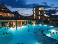 Wieczorem w hotelu przy termach chochołowskich, ludzie relaksują się w podświetlonym basenie z wodnymi zjeżdżalniami w tle.