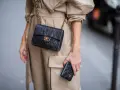 Elegancka kobieta w beżowym płaszczu prezentuje klasyczną, pikowaną torebkę Chanel vintage z złotym łańcuszkiem i logo.