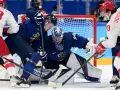 Bramkarz Finlandii broni strzał. W tle zawodnicy walczą o krążek, dążąc do zwycięstwa, jak przystało na mistrzów olimpijskich w hokeju na lodzie.