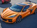 Pomarańczowy Chevrolet Corvette C8 z czarnym dachem i spojlerem na torze wyścigowym. Obok widać fragment czerwonego samochodu.