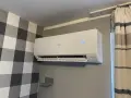 Biała klimatyzacja Haier zamontowana na szarej ścianie, obok wzorzystej tapety i zasłon.