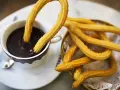 Churros sin gluten dorados y crujientes, uno sumergido en chocolate caliente, otro en una cesta.