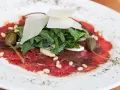 Delicato carpaccio di manzo con rucola, scaglie di parmigiano, pinoli, capperi e funghi.