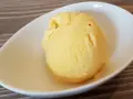 Ein Löffel cremiges, gelbes balla balla Eis in einer weißen Schale auf Holzhintergrund.