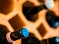 Wino w butelkach leżakuje w drewnianym stojaku. Prawidłowe przechowywanie wina w butelkach zapewnia jego jakość.