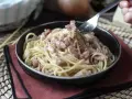 Un tenedor recoge espaguetis cremosos con trozos de bacon crujiente, creando un delicioso plato de pasta con bacon.