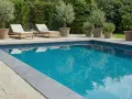Luxuriöser Pool mit Steinumrandung und mediterranen Pflanzen. Tolle pool verkleiden ideen für eine elegante Poollandschaft.
