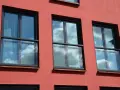 Trzy nowoczesne okna z czarnymi ramami i żaluzjami, odbijające błękitne niebo z chmurami. Wyglądają jak małe balkony francuskie.