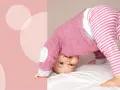 Dziecko w piżamce próbuje raczkować, wyginając się w łuk. Wesoła mina sugeruje, że to świetna zabawa i sposób, jak pomóc dziecku raczkować.