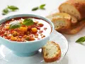 Zupa jarzynowa a minestrone w niebieskiej miseczce, udekorowana bazylią, podana z chrupiącym pieczywem.