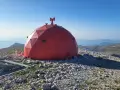 Struttura rossa a cupola su un terreno roccioso, con vista panoramica sulle montagne del Monte Amaro.
