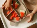 Kleine Hände greifen nach saftigen Wassermelone-Stücken auf einem Teller. Ein süßer Wassermelone-Baby-Moment.