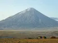 Ol Doinyo Lengai, wulkan w Tanzanii, góruje nad sawanną z kilkoma tradycyjnymi chatami Masajów.