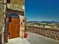 Un portone in legno in un borgo toscano, con vista panoramica sulle colline. Perfetto per un tour in moto tra i borghi più belli della Toscana.