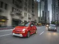 Czerwony Fiat 500e jedzie ulicą w mieście, w tle wieżowce i autobus.