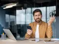 Zdezorientowany mężczyzna trzyma telefon, jakby właśnie dowiedział się o problemach z cesją.