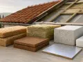 Vari materiali isolanti, tra cui pannelli per rasante termico per esterno, disposti davanti a un tetto in fase di ristrutturazione.