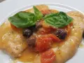 Delizioso pollo alla mediterranea con pomodorini, olive nere e basilico fresco su un piatto bianco.