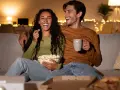 Ein lachendes Paar genießt einen gemütlichen Filmabend mit Popcorn und Pizza. Perfekte filmabend snacks für einen entspannten Abend.