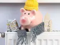Świnka-skarbonka w czapce i szaliku, z banknotami i domkami na grzejniku. Oszczędzanie na rachunki za ogrzewanie, czyli bon ciepłowniczy w praktyce.