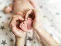 Dłonie obejmujące stópki 7 tygodniowego dziecka. Delikatne paluszki i pięty maluszka otoczone troską.