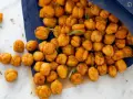 Un sacchetto blu rovesciato rivela una montagna di ceci croccanti al forno, dorati e invitanti, con qualche rametto di rosmarino sparso tra loro.